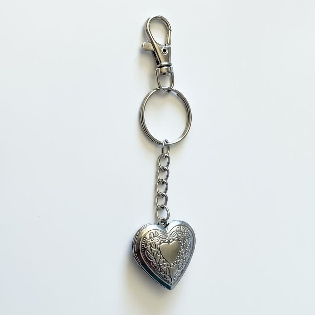 A silver-toned metal keychain featuring a lobster clasp, split key ring, and an ornate heart-shaped locket pendant with a smaller heart in the center, shown on a plain white background.