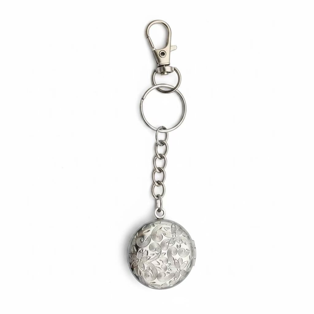A silver metal keychain featuring a round, intricately carved floral round locket pendant, attached to a short chain, split ring, and lobster clasp, shown on a plain white background.
