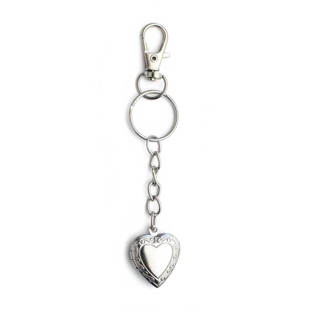 A silver-toned metal keychain featuring a lobster clasp, a split key ring, a short chain, and an ornate heart-shaped locket pendant with engraved detailing, shown on a plain white background.