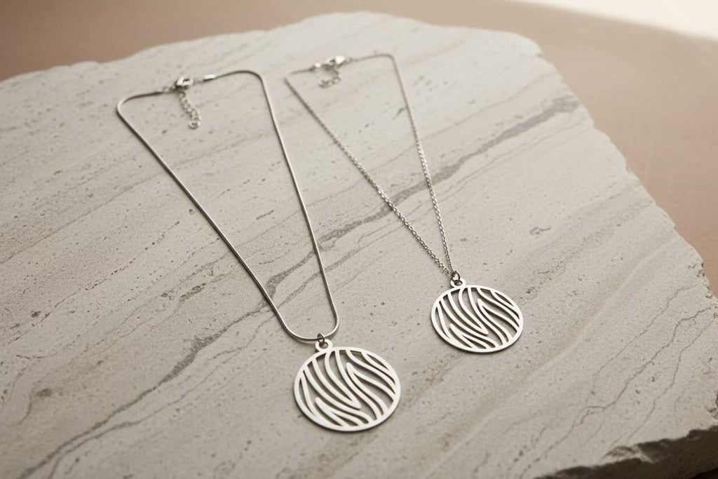 Two silver pendant necklaces with circular flame stripe cutout pendants, displayed on a textured light gray stone slab.