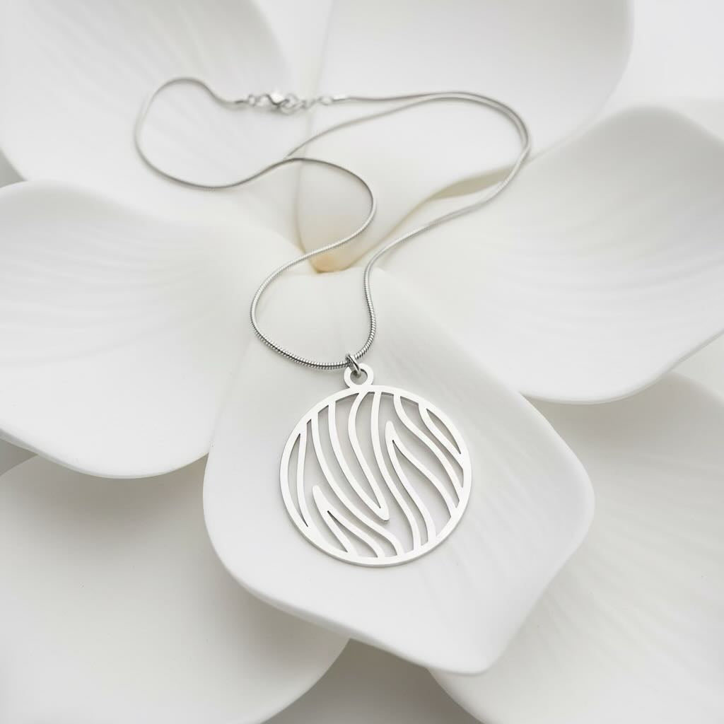 A silver necklace with a circular pendant featuring a flame cutout pattern, displayed on a large white flower.