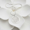 A silver necklace with a circular pendant featuring a flame cutout pattern, displayed on a large white flower.