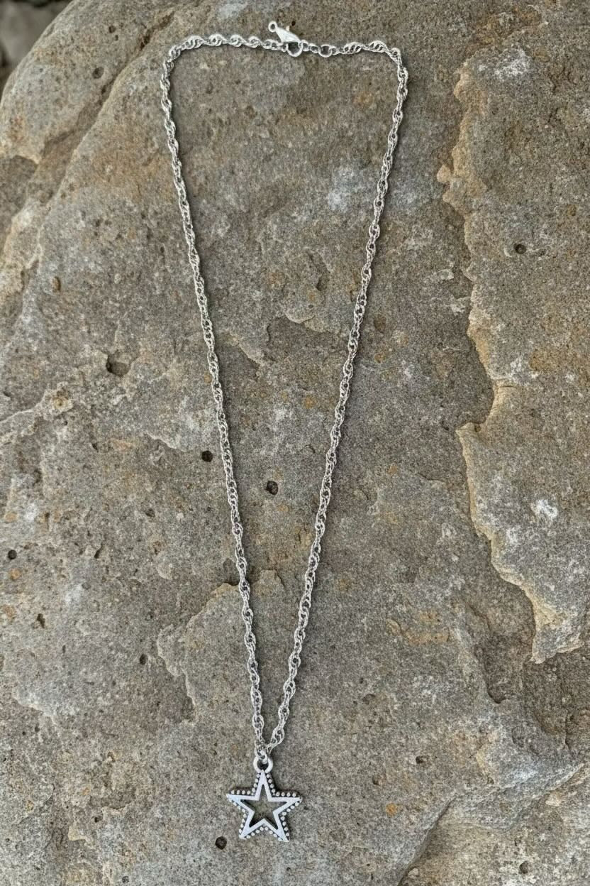 A silver-toned chain necklace with a dangling star charm, laid out on a textured gray stone surface.