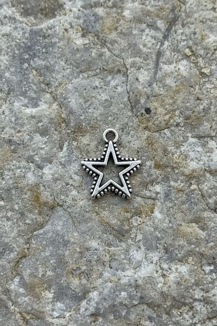 A silver-toned five-pointed star charm with a beaded border and a top loop, resting on a textured gray stone surface.