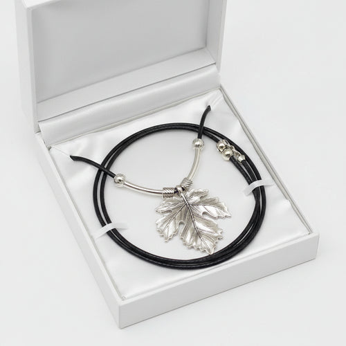 A silver leaf pendant necklace on a black cord, displayed in a white gift box.
