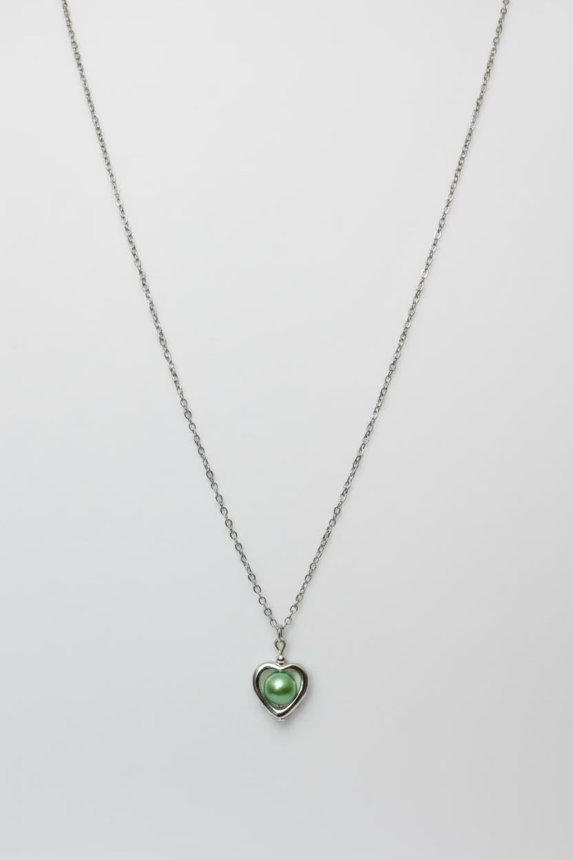 A silver chain necklace with a small heart-shaped pendant featuring a light sea green pearl, displayed against a plain light gray background.