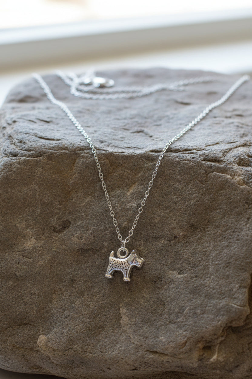A silver-tone chain necklace with a small dog-shaped pendant, displayed on a large stone.