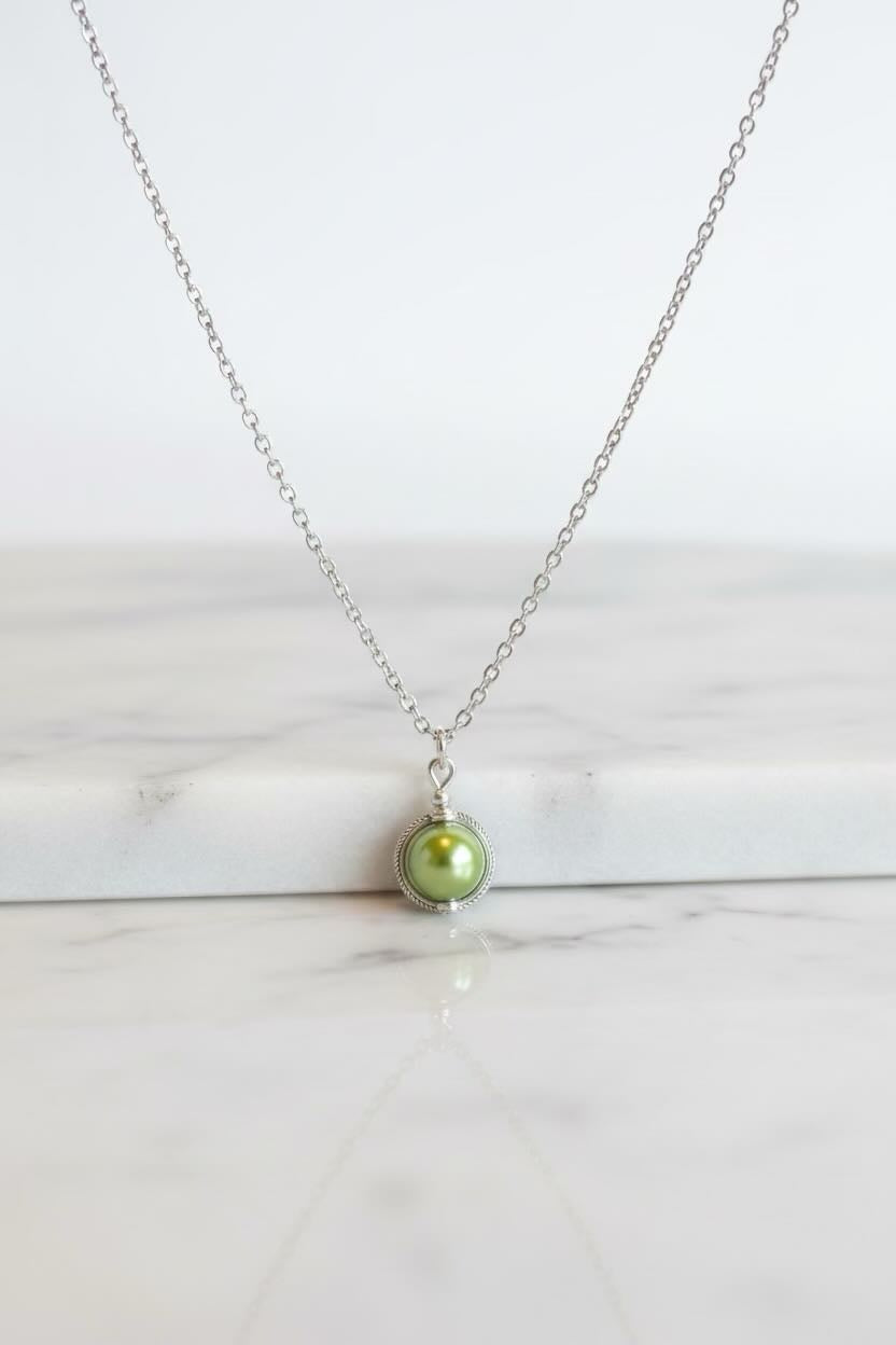 A delicate silver chain necklace with a single round sea green pearl pendant, displayed on a white marble surface against a white background.