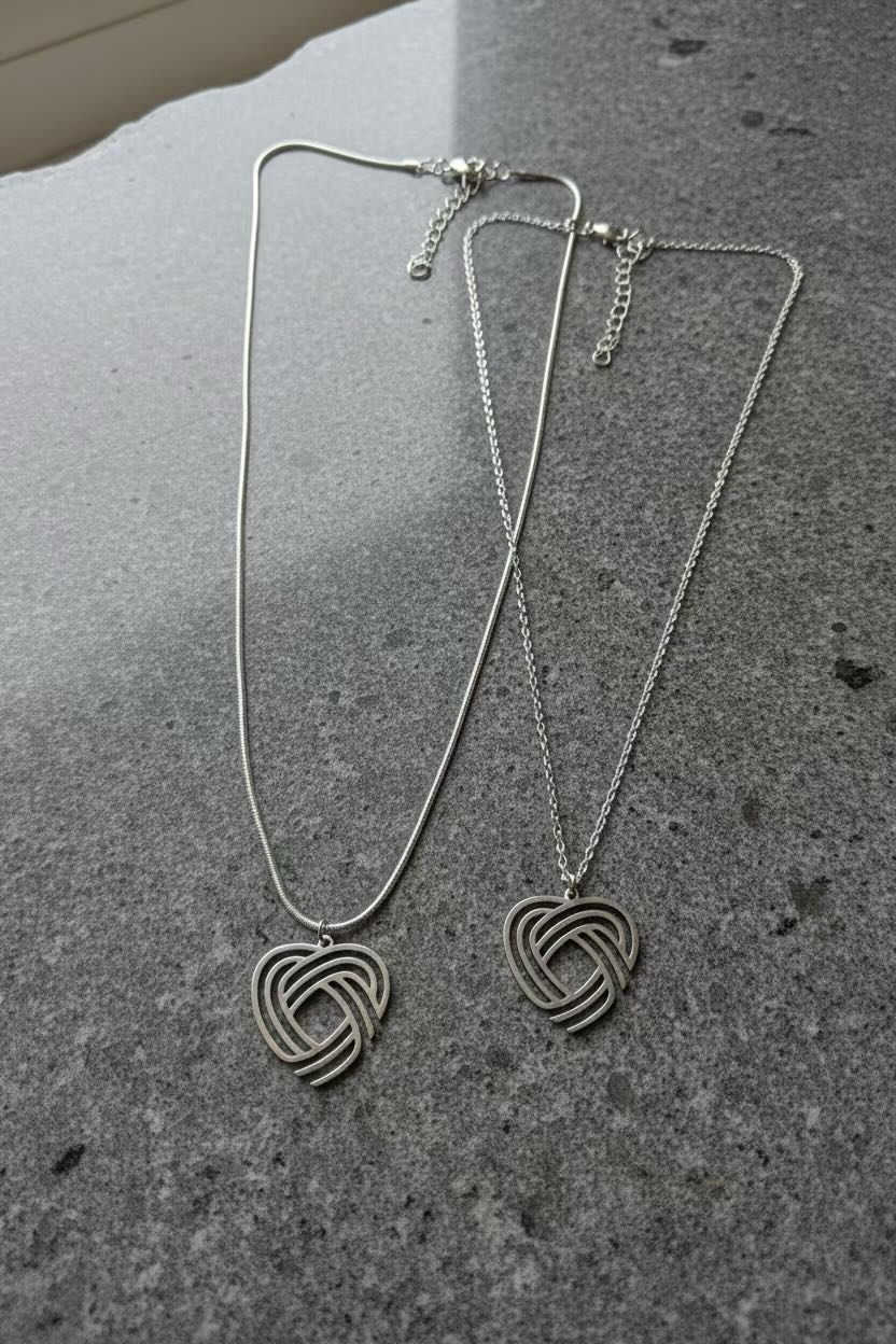 Two silver-toned interlocking heart pendant necklaces on delicate chains, displayed on a textured gray stone surface.