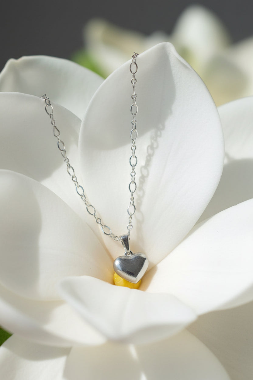 A silver heart pendant necklace displayed on a white large flower
