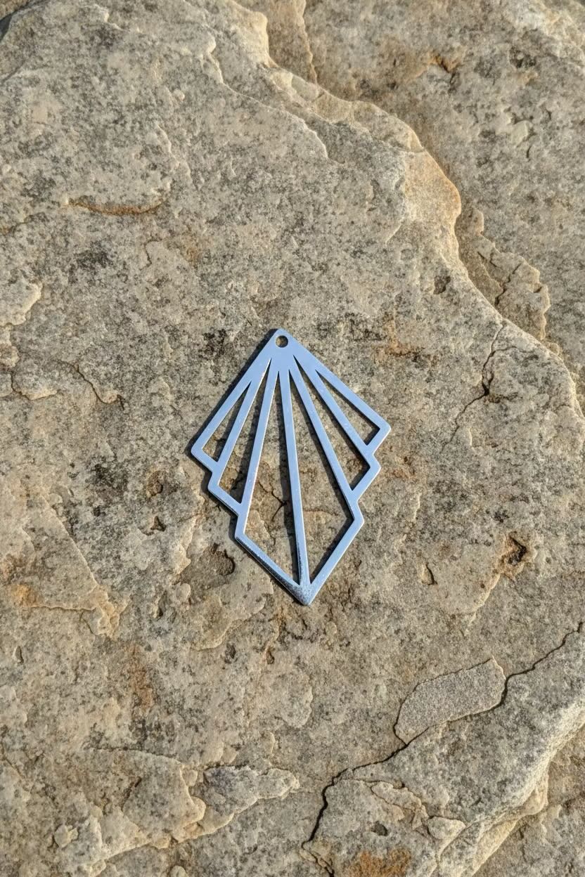 A silver metal art deco fan pendant with a fan-like cutout design, resting on a textured natural stone surface.