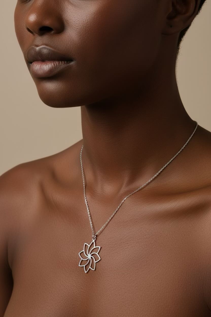 A close-up of a model wearing a delicate silver chain necklace with a flower-shaped pendant, set against a warm beige background.