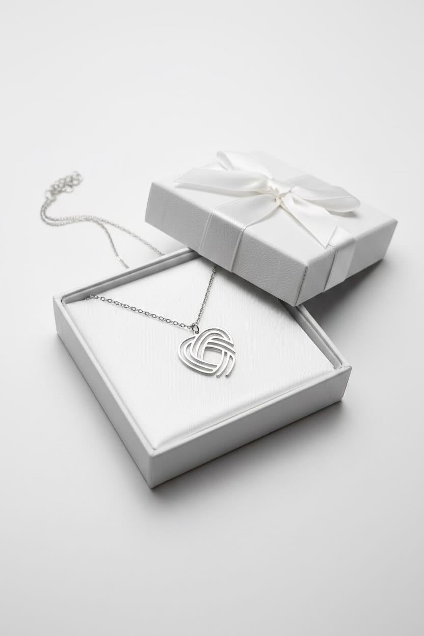 A silver heart-shaped pendant necklace with an interlocking knot design, displayed inside an open white gift box with a matching closed box and ribbon on a light gray background.