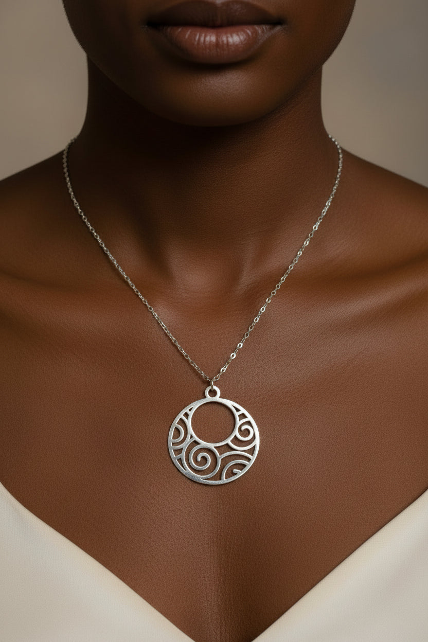 A silver pendant necklace with a circular cutout design featuring swirl patterns, displayed on a model.