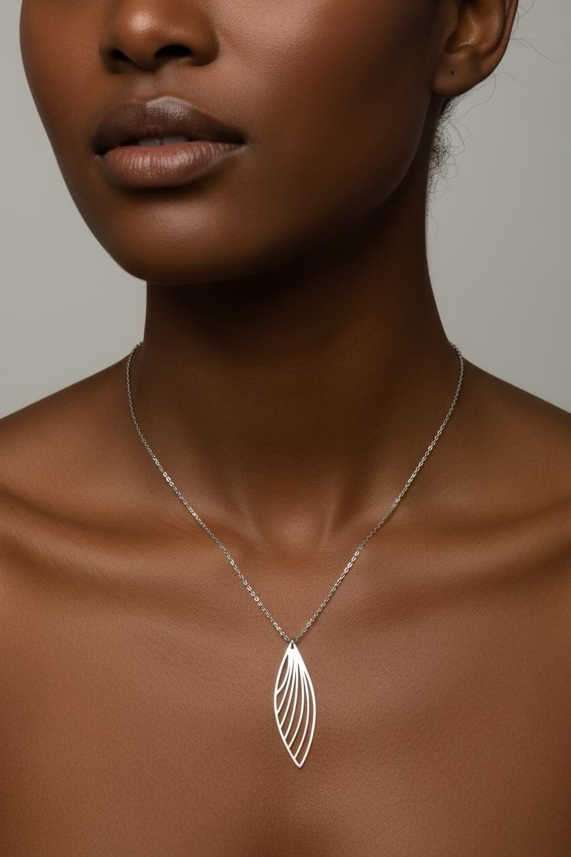 A close-up of a model wearing a delicate silver chain necklace with a feather wing-shaped pendant, set against a neutral gray background.