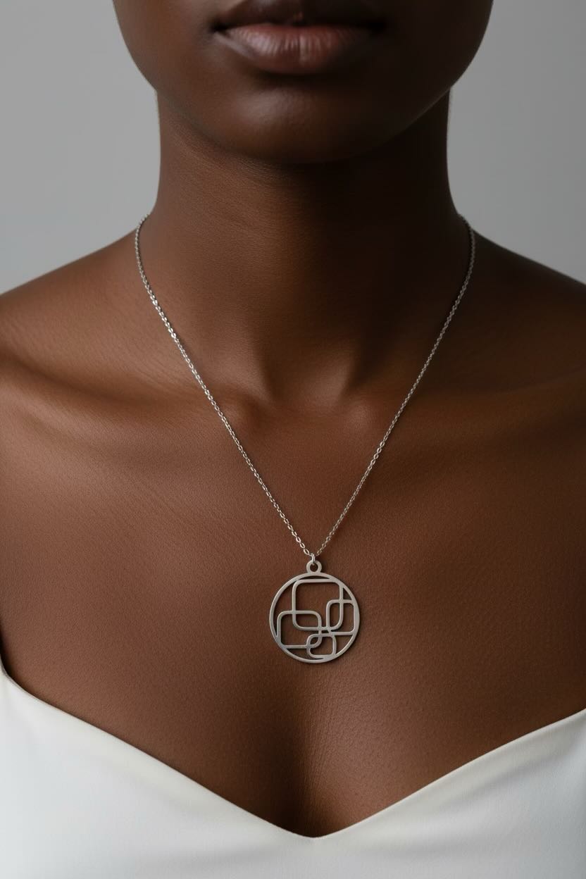 A close-up of a model wearing a delicate silver chain necklace with a circular pendant featuring an interlocking geometric design.