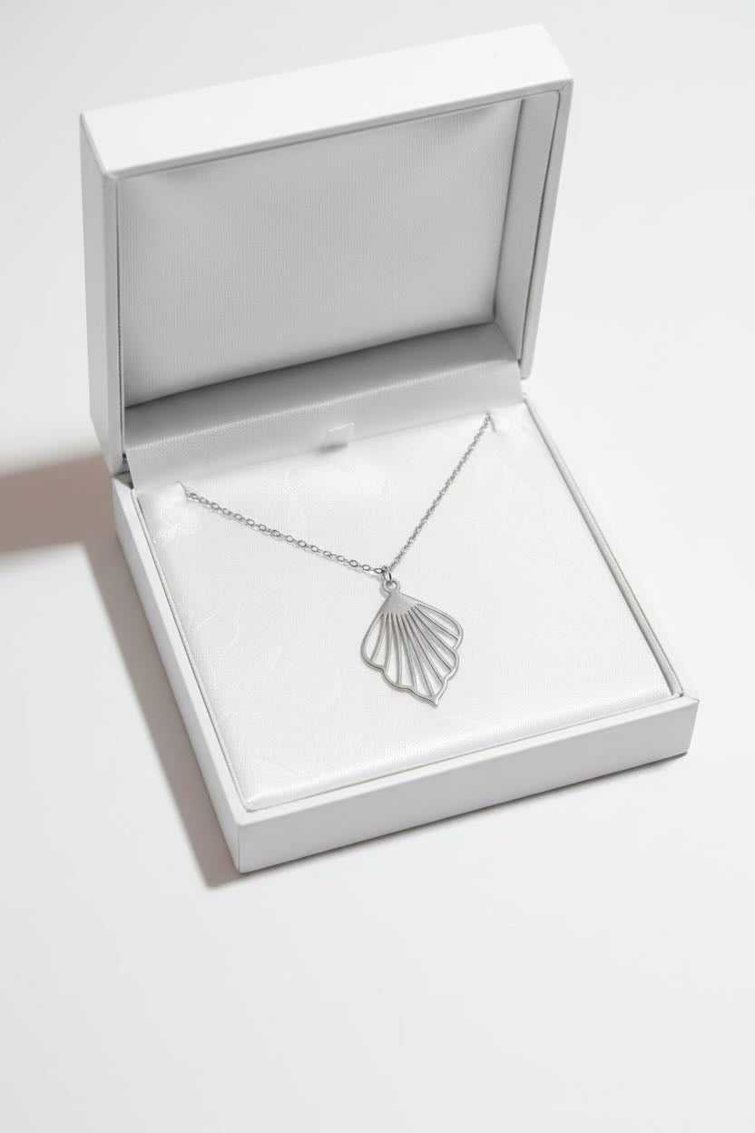 A silver ginkgo fan-shaped pendant necklace on a delicate chain, presented inside an open white jewelry box with a white cushion.