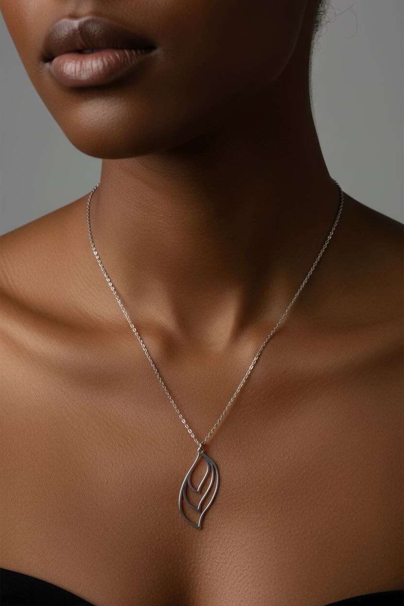 A close-up of a model wearing a delicate silver chain necklace with a stylized, openwork leaf or flame-shaped pendant.