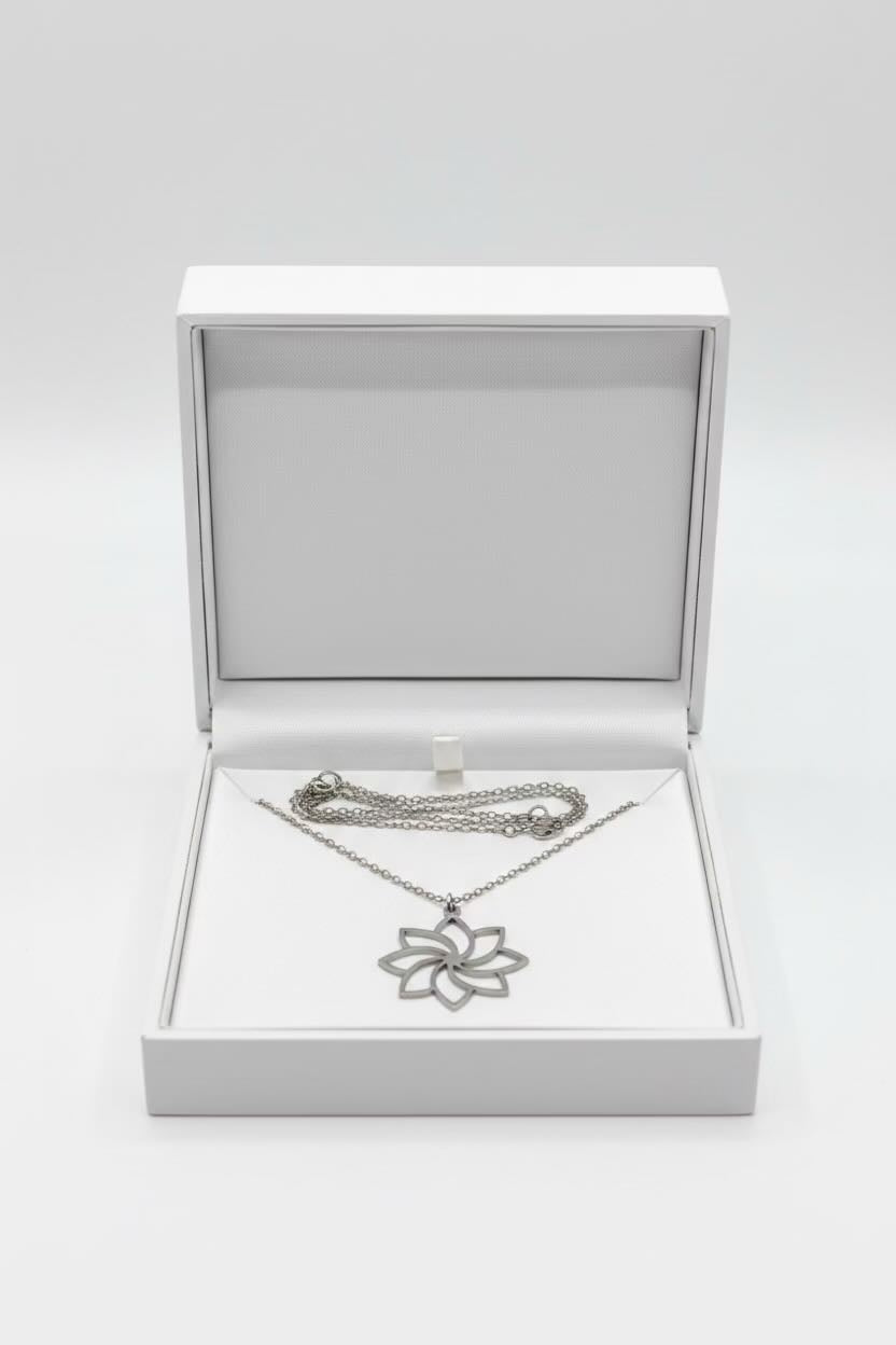 A silver-toned flower-shaped pendant necklace displayed inside an open white jewelry box on a light gray background.