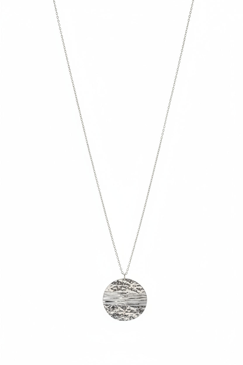 A silver-toned necklace with a round, textured pendant displayed hanging down with a white background.
