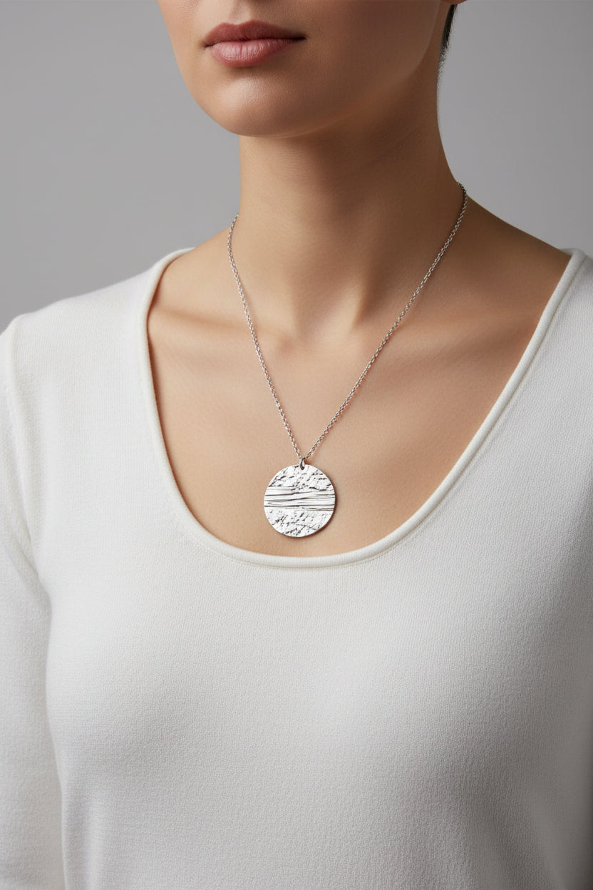 A silver-toned necklace with a round, textured pendant displayed on a model.