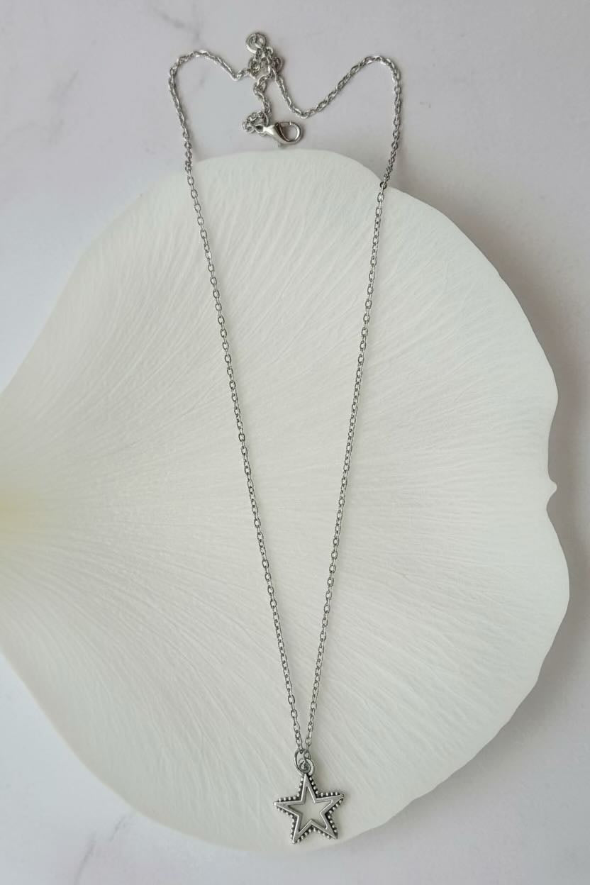 A delicate silver chain necklace with a small star-shaped pendant, displayed on a large white petal-shaped dish against a light background.