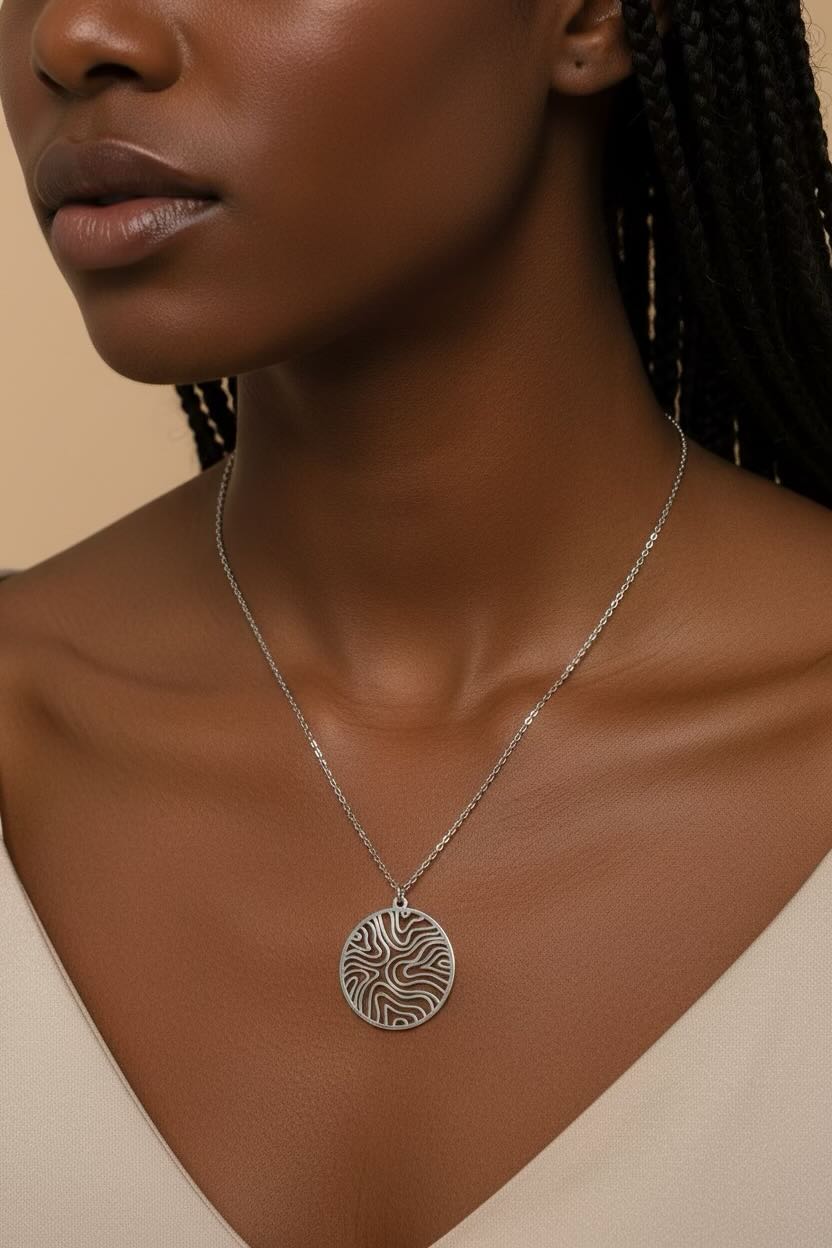 A close-up of a model wearing a silver pendant necklace with a circular, wave pattern circle patterned pendant on a delicate silver chain.