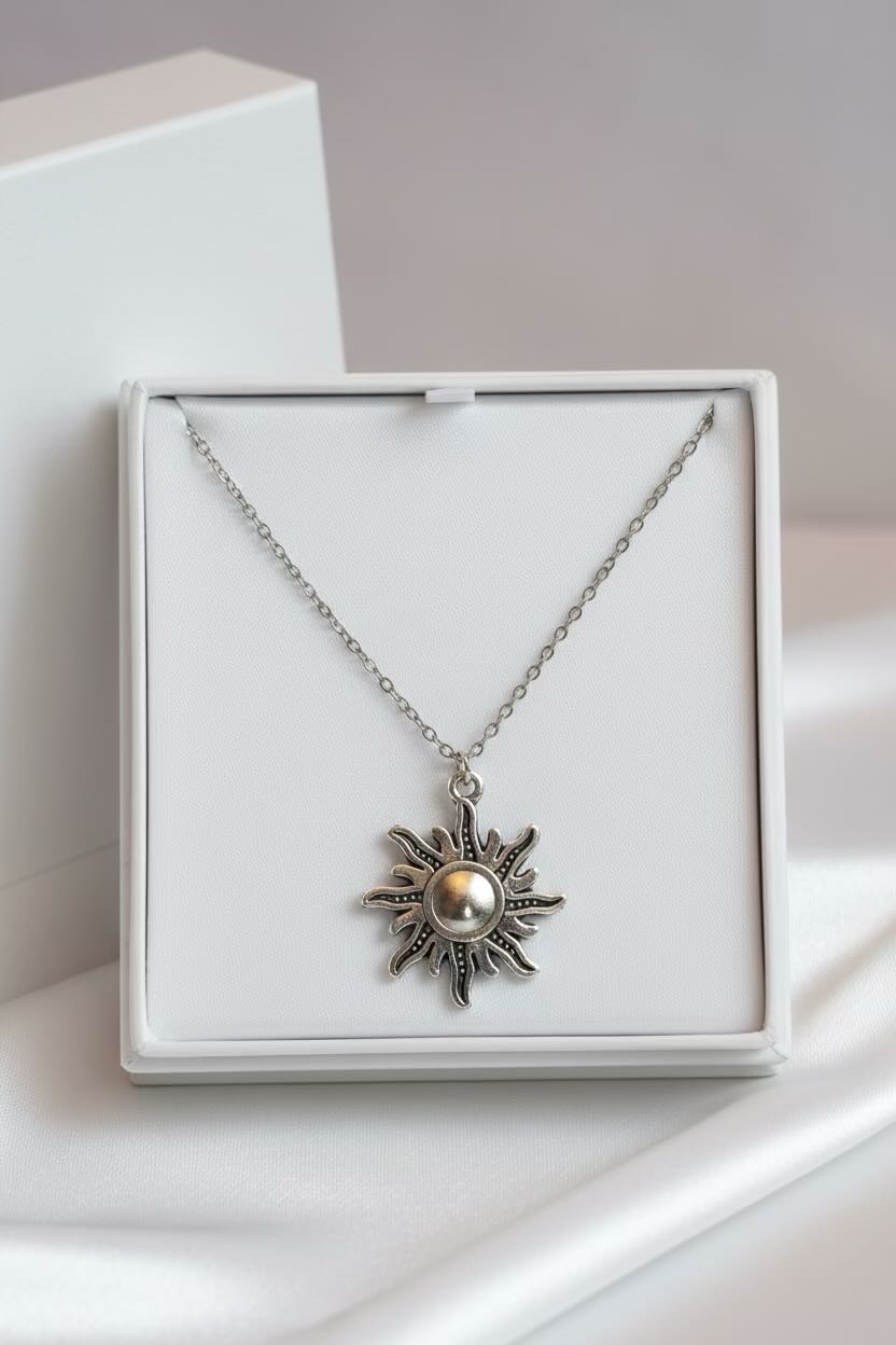 A silver sunburst pendant necklace with a central pearl, presented in a white square gift box on a soft white background.