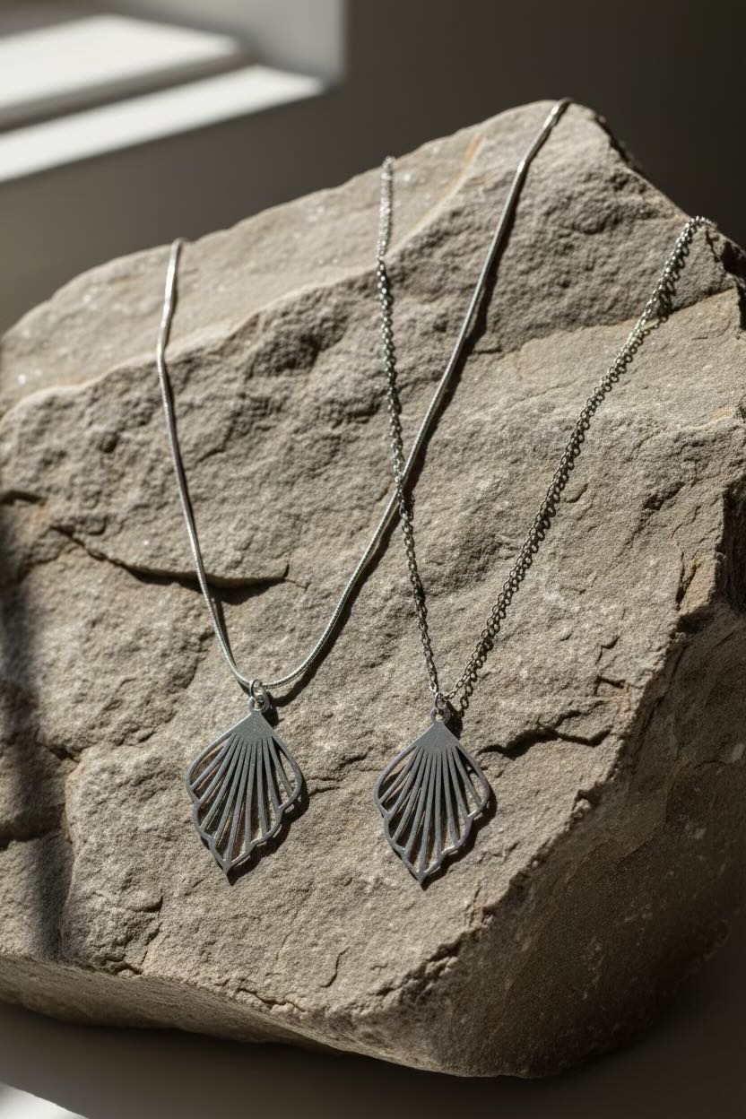 Two dark metal ginkgo fan-shaped pendant necklaces displayed on a rough stone surface in natural light.