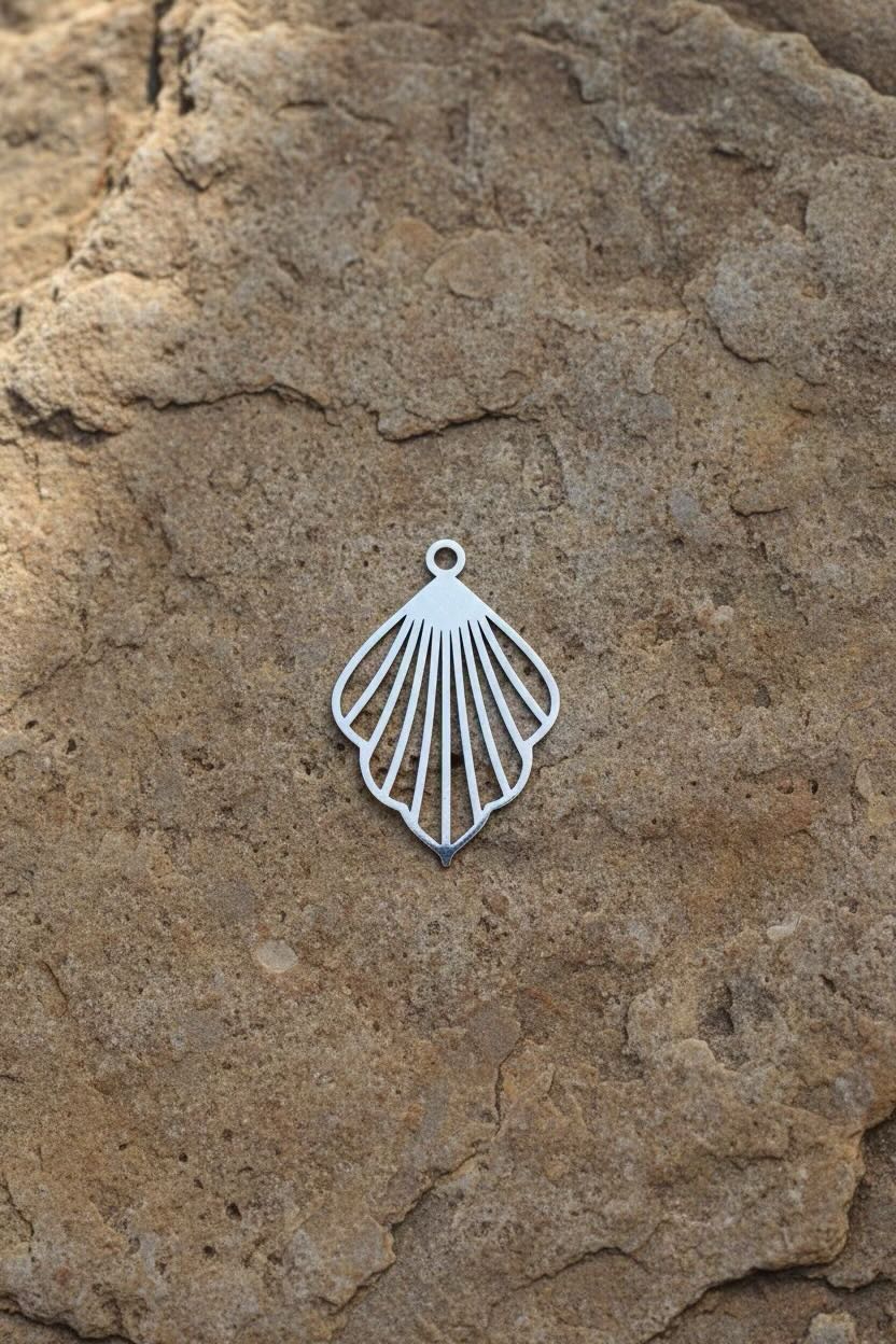 A silver metal ginkgo fan-shaped pendant with a fan-like cutout design, resting on a textured brown rock surface.
