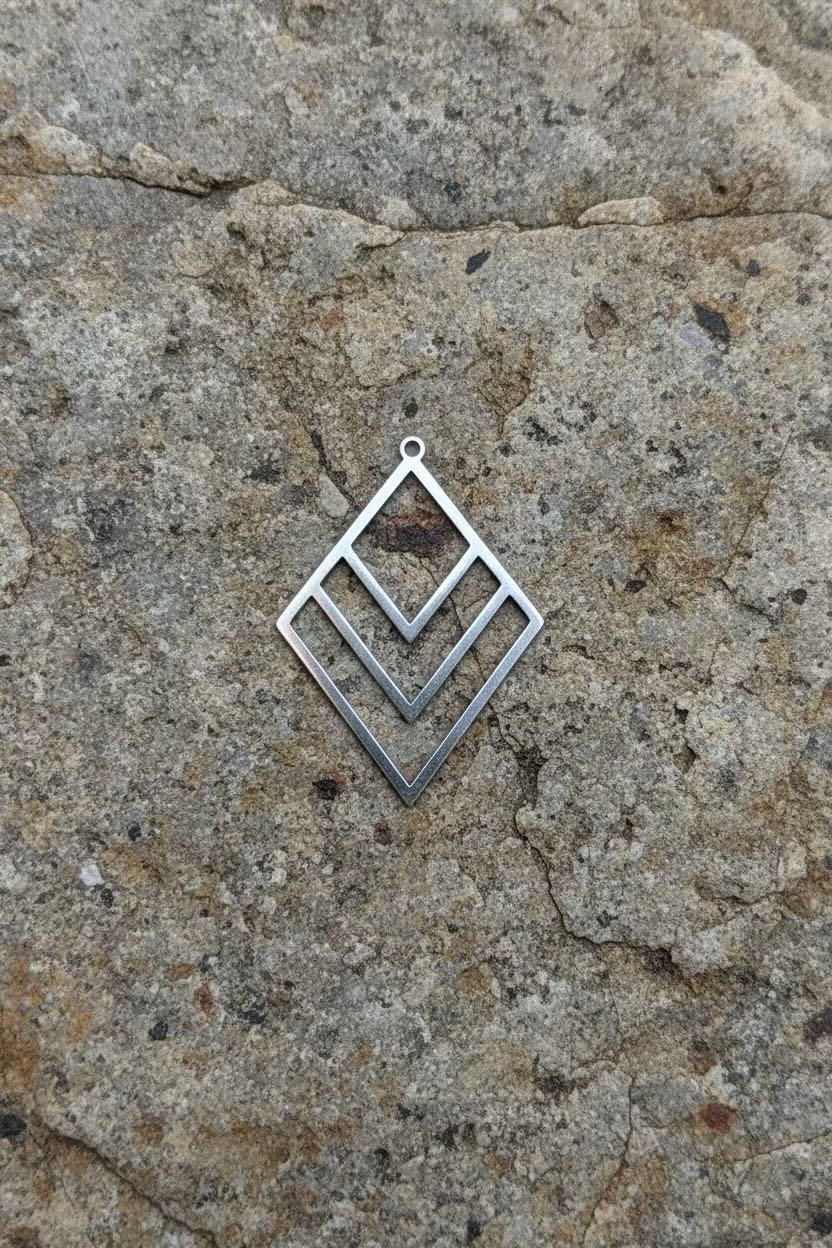 A silver geometric diamond-shaped pendant with an open chevron design, resting on a textured gray stone surface.