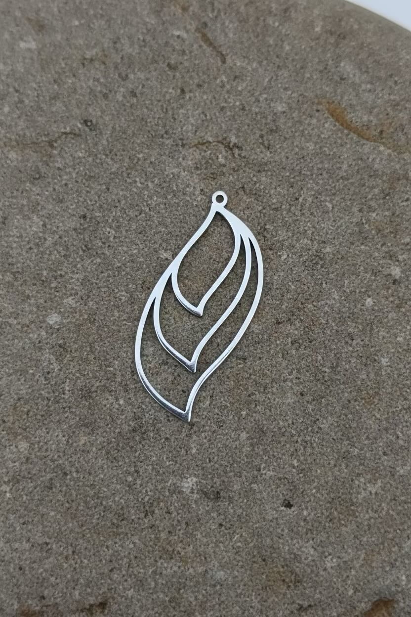 A silver-toned metal pendant with an abstract, layered leaf or feather-like cutout design, resting on a textured gray stone surface.