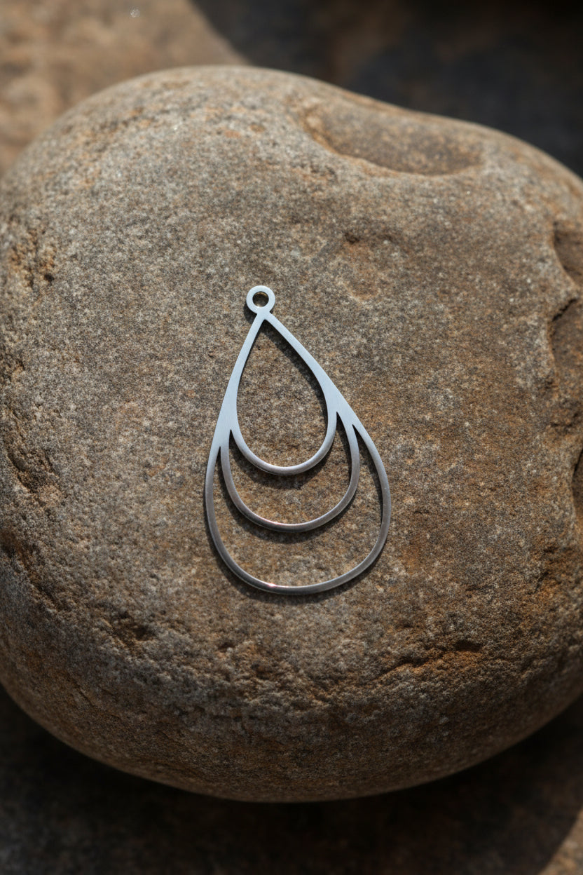 A silver teardrop-shaped pendant on a brown stone