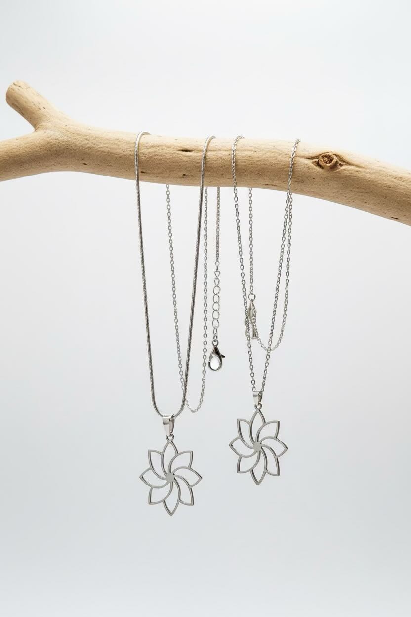 Three silver-toned chain necklaces with flower-shaped pendants displayed on a light wood branch against a white background.