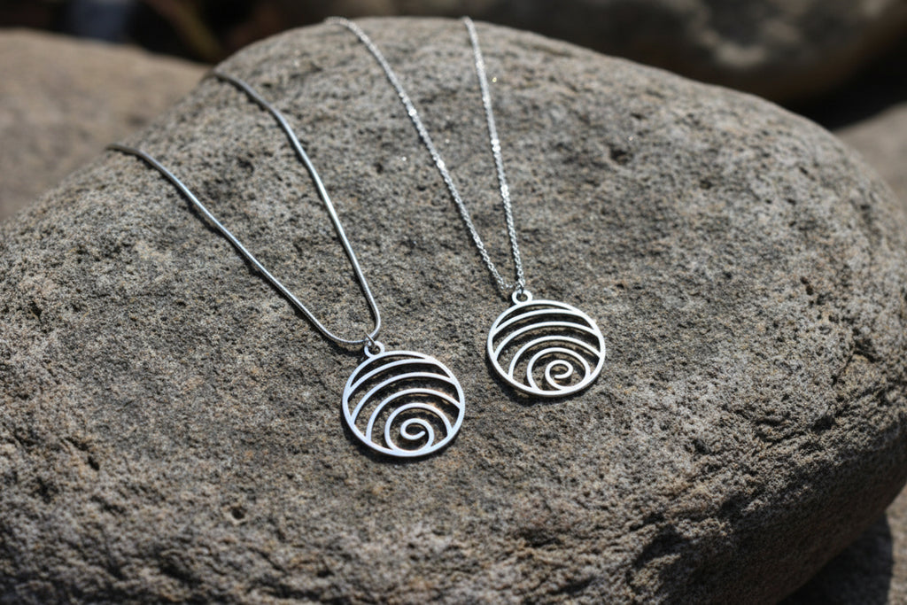 Two silver spiral pendant necklaces displayed on a textured gray rock.