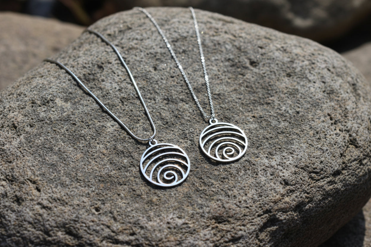 Two silver spiral pendant necklaces displayed on a textured gray rock.