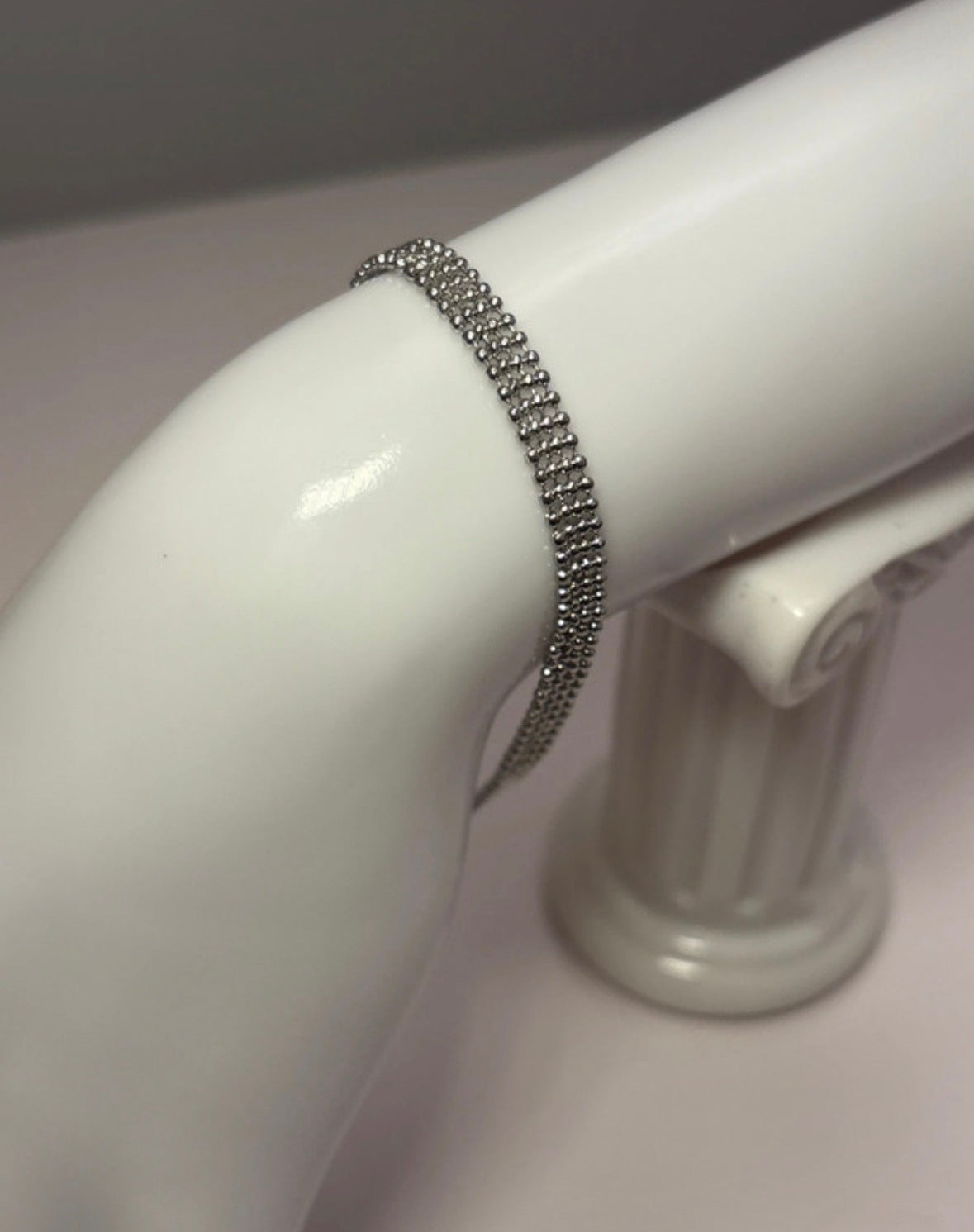Silver bracelet on a white mannequin arm against a neutral background