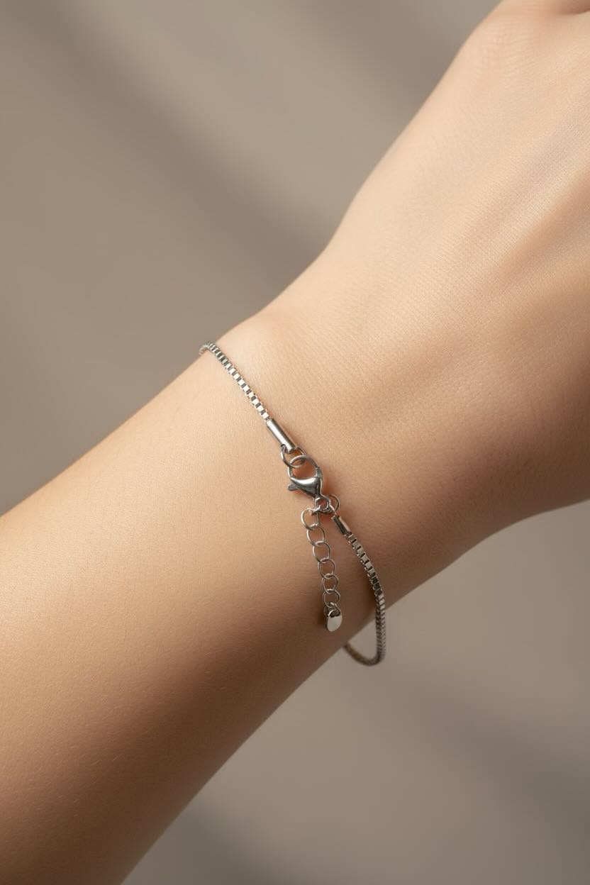 A delicate silver chain bracelet with a small bow charm and extension chain, shown worn on a person's wrist against a soft neutral background.