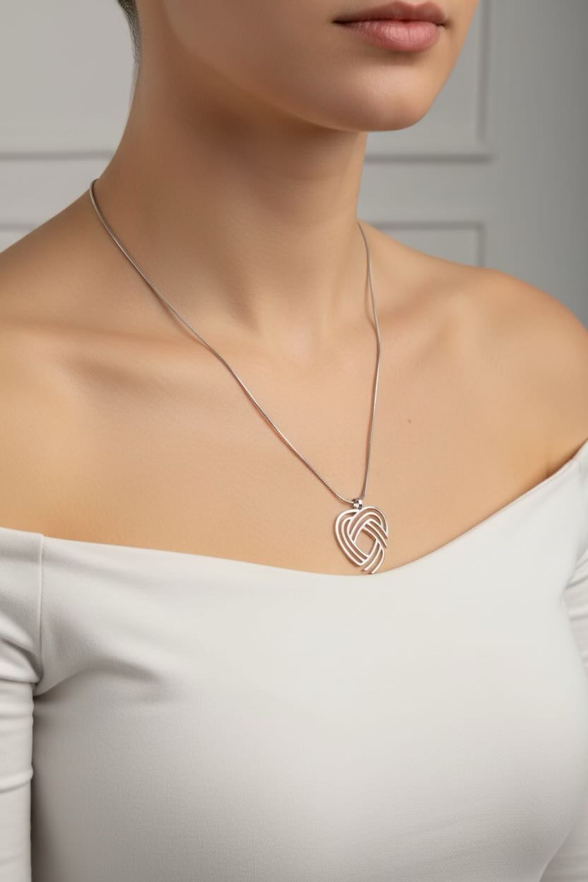 A close-up of a woman wearing a delicate silver necklace with an Celtic love knot heart pendant, styled with a white off-the-shoulder top.