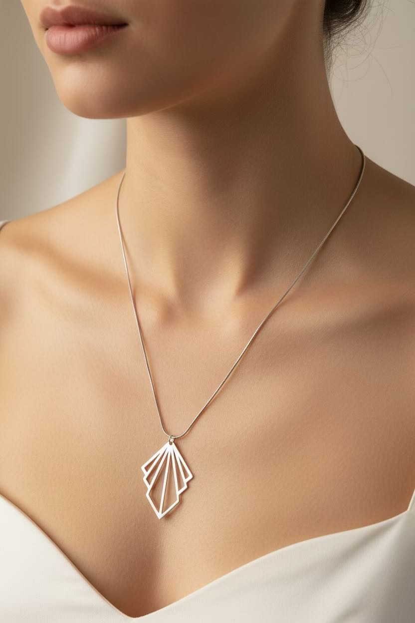 A close-up of a woman wearing a delicate silver necklace with a geometric, fan-like pendant over a white top.