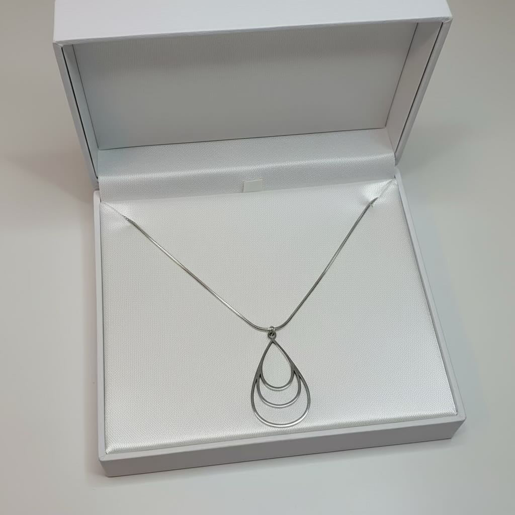 A silver-toned teardrop pendant necklace with a thin chain, displayed inside an open white jewelry box with a satin-lined insert.