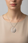 A silver circular pendant necklace with an openwork scroll pattern, displayed on a model.