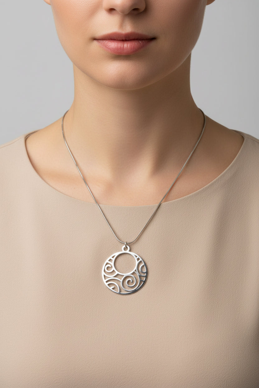 A silver circular pendant necklace with an openwork scroll pattern, displayed on a model.