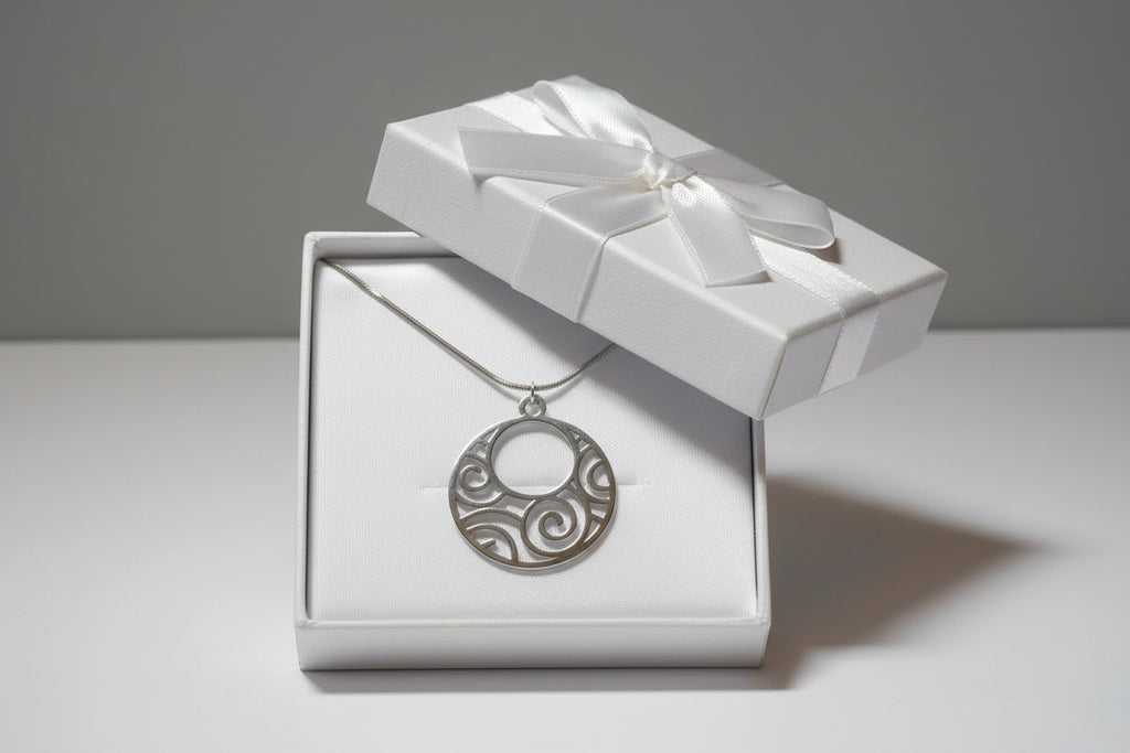 A silver circular pendant necklace with an openwork scroll pattern, displayed in a white gift box.