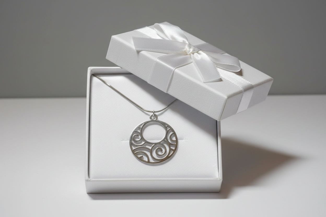 A silver circular pendant necklace with an openwork scroll pattern, displayed in a white gift box.