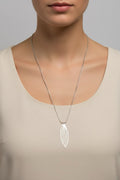 A silver feather wing-shaped pendant necklace worn by a model in a beige top against a neutral gray background.