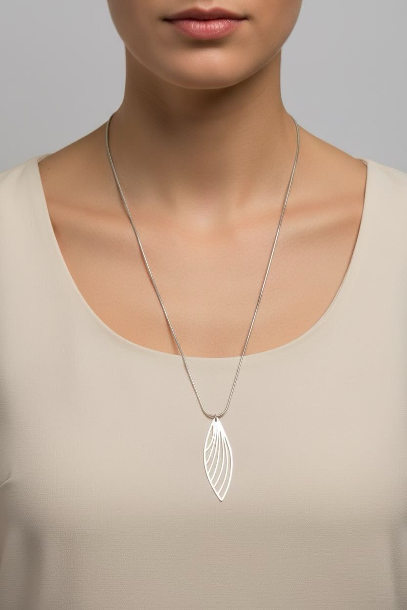 A silver feather wing-shaped pendant necklace worn by a model in a beige top against a neutral gray background.