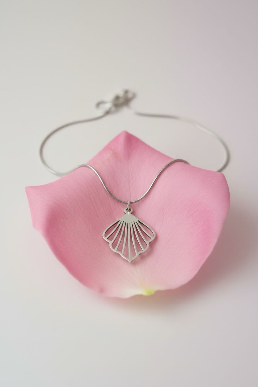 A silver ginkgo fan-shaped pendant necklace resting on a pink rose petal against a soft white background.