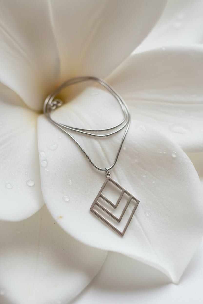 A silver layered diamond chevron pendant necklace resting on large white flower petals with water droplets.
