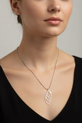 A close-up of a woman wearing a delicate silver necklace with a stylized leaf pendant, paired with a black V-neck top against a neutral gray background.